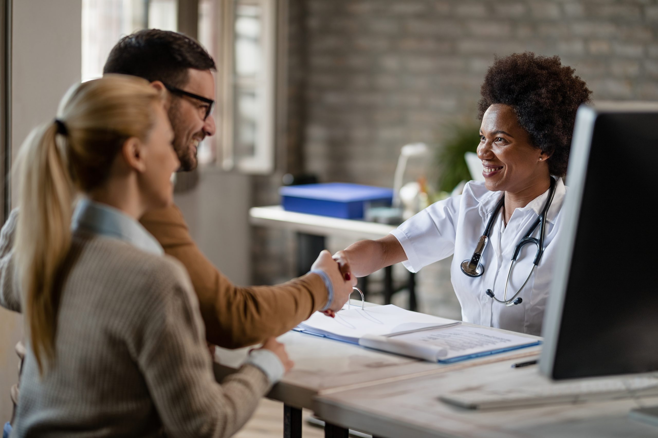 Casal feliz apertando a mão de uma médica após as consultas na clínica.